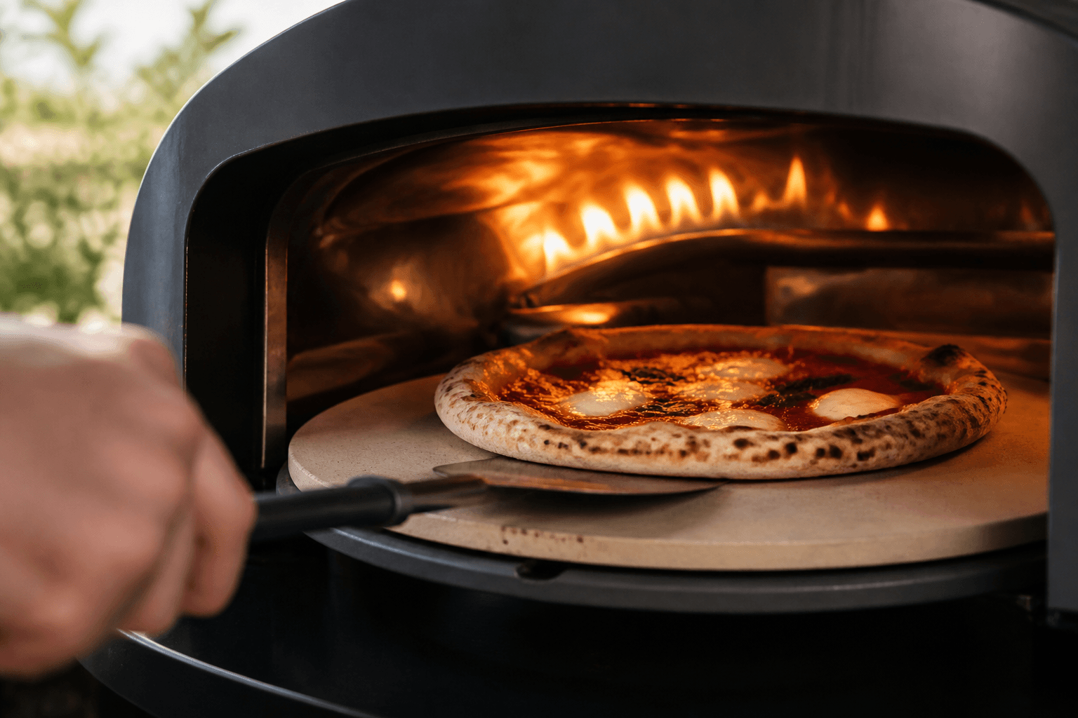 Piedra refractaria giratoria cocinando una pizza bajo una llama lateral